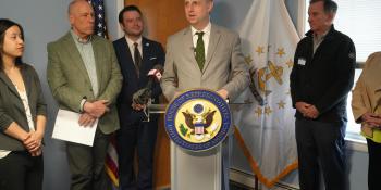 Magaziner speaks at a podium surrounded by leaders at South Kingstown Housing Authority