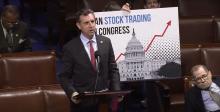 Magaziner stands on House floor in front of sign that reads, "Ban Stock Trading for Congress"
